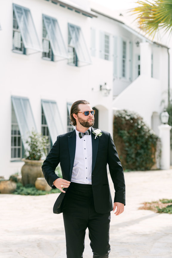 Handsome groom walking with sunglasses on in Alys Beach. Florida for his destination beach wedding. Alys Beach wedding photography by Heather Durham.