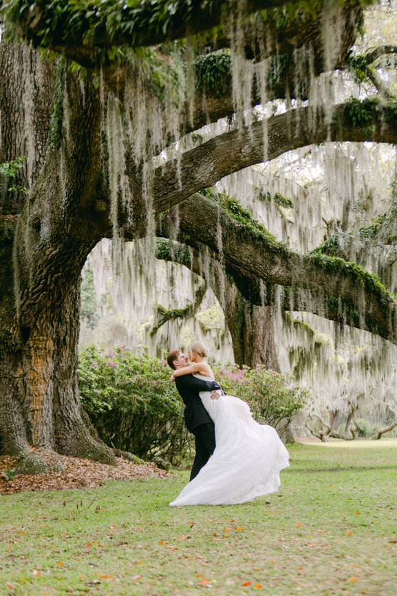 Groom and groom hugging and kissing in front of a live oak tree with hanging moss after their ceremony in Savannah, Georgia. Destination wedding photography by Heather Durham.