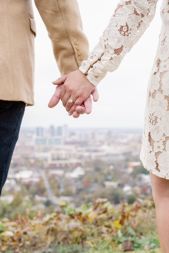 Engaged couple showing ring in front of Birmingham, Alabama city skyline. Engagement shoot by Heather Durham Photography.