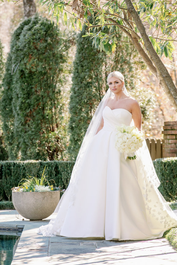Sophisticated bride in Sareh Nouri dress standing poolside with all white bridal bouquet. Luxury Alabama wedding photography by Heather Durham.