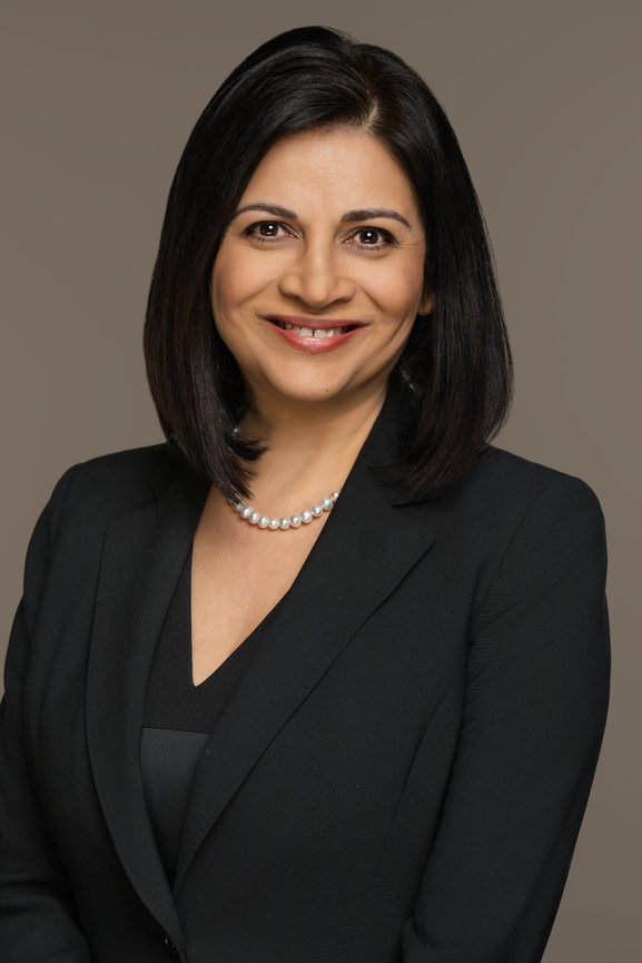 Professional portrait of a woman with shoulder-length black hair, wearing a black suit and pearl necklace, smiling.