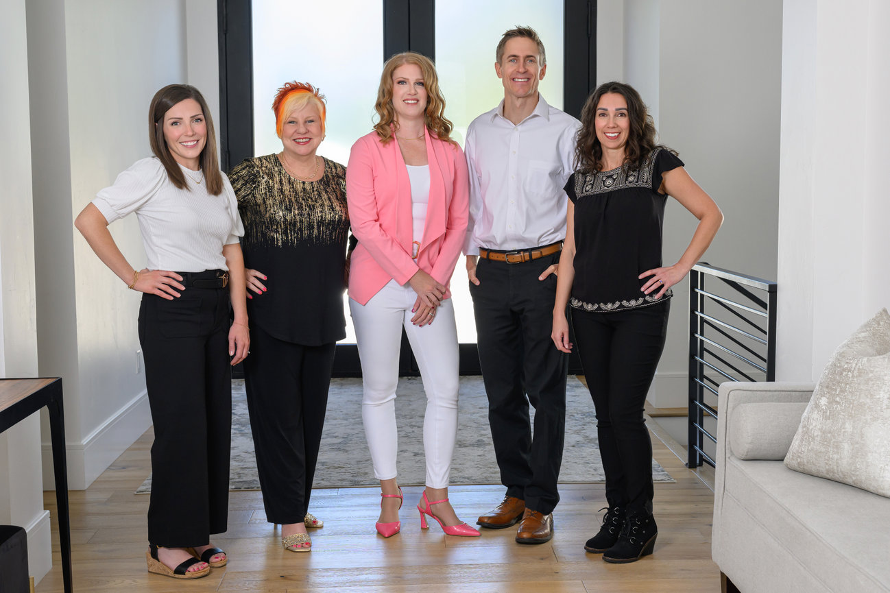 Five people standing in a well-lit room, smiling and posing together.