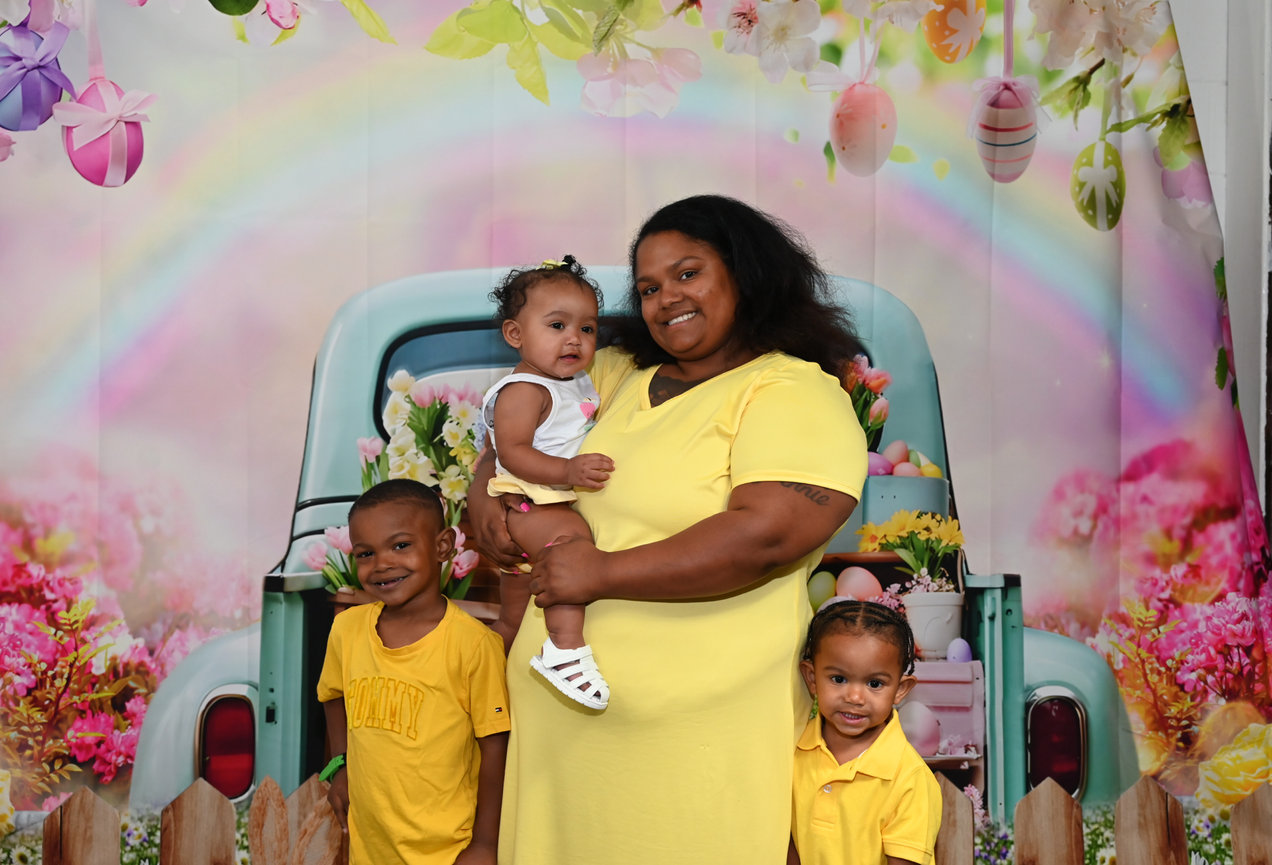 Mother holding a baby surrounded by three children at a colorful celebration