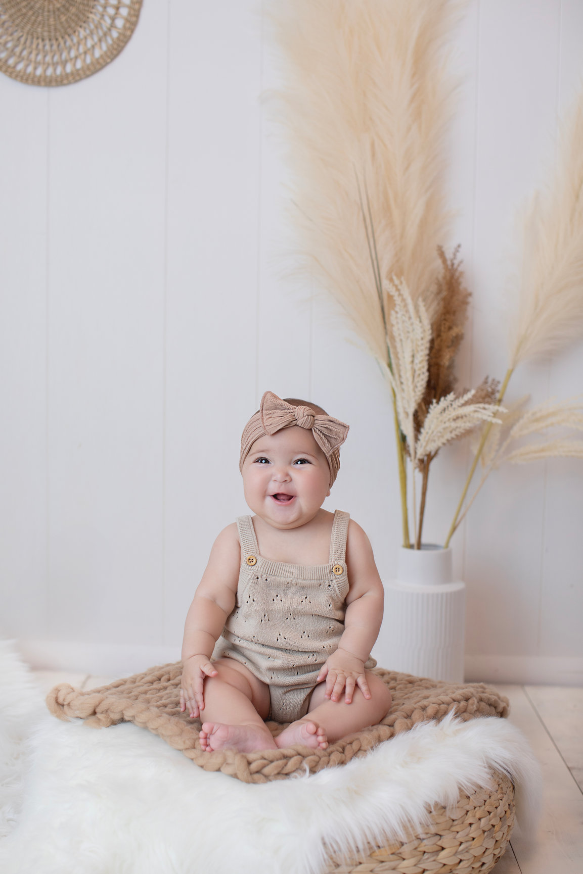 Baby sitting beside dried grasses in a neutral studio set