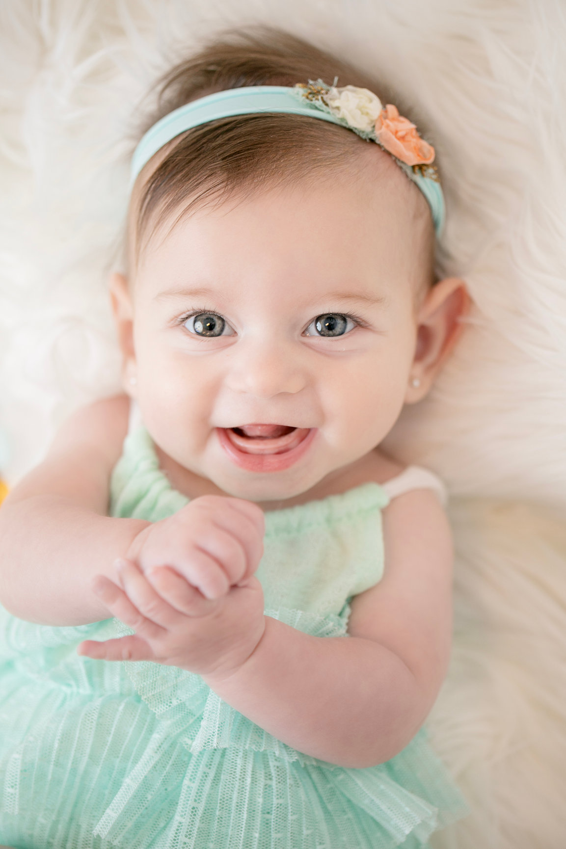 Smiling baby wearing a mint dress and a small floral headband.