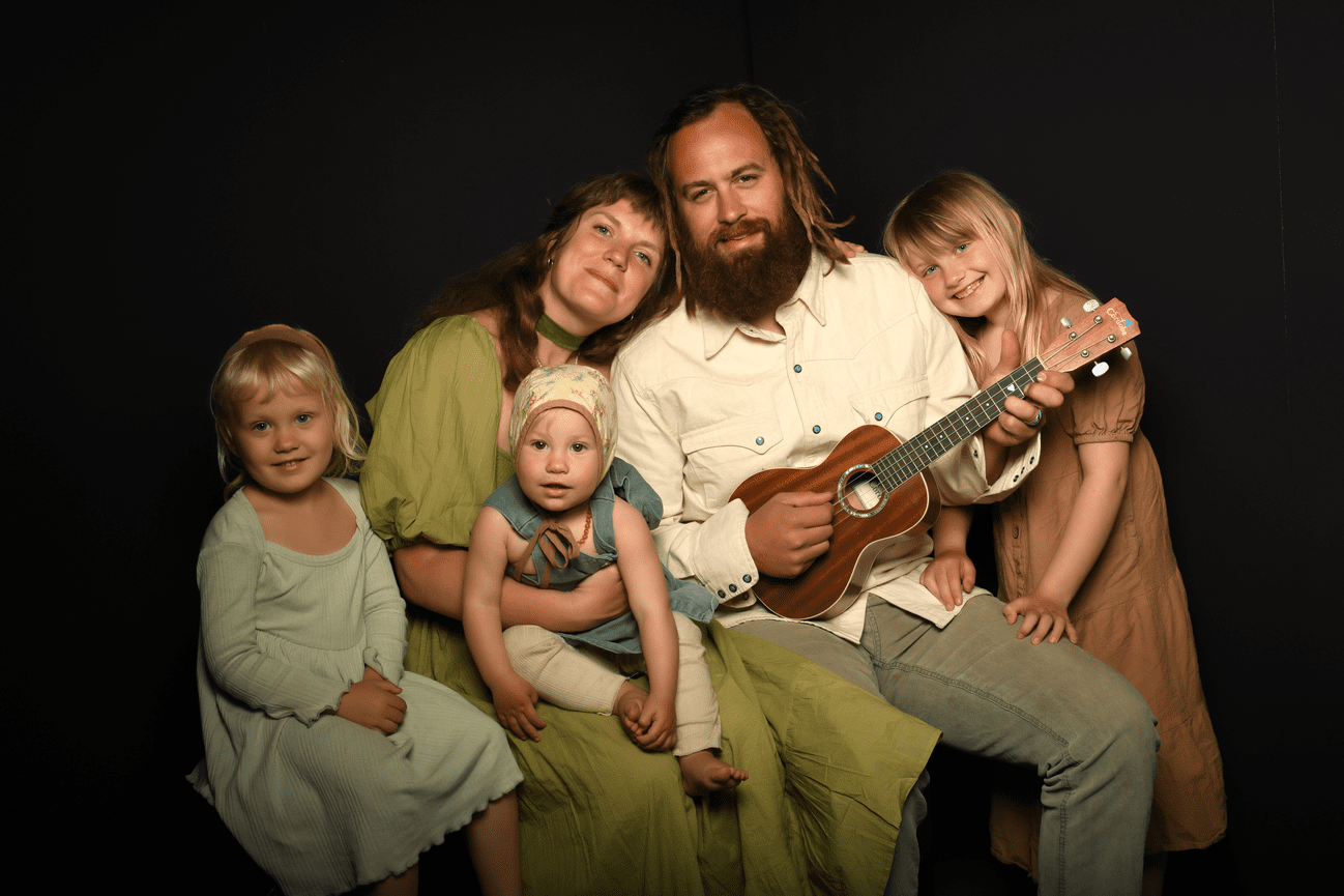 Parents with their three girls all wearing organic fabrics and dad holding a ukulele.