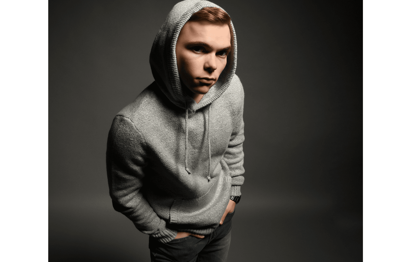 A senior boy wearing his hood over his head looks seriously into the camera.