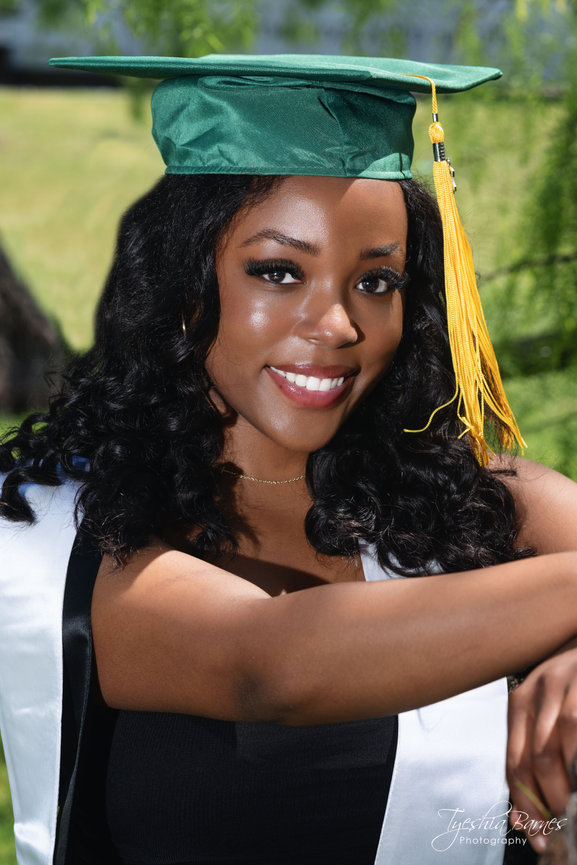 Smiling graduate in cap and gown tossing hat outdoors in Dallas.