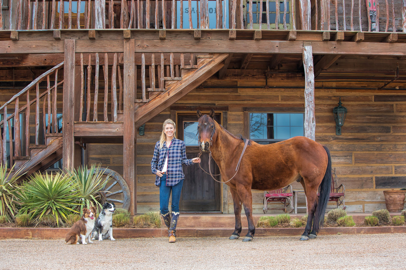 Portrait of a woman with her horse and two dogs in front of a barn.
