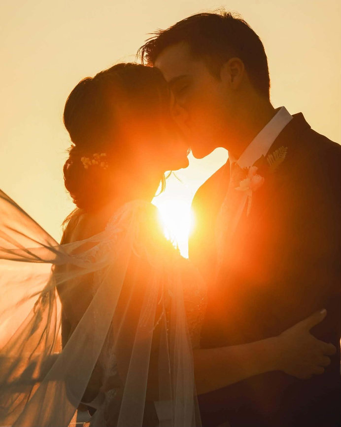 Bride and groom embracing with the sun shining between them.