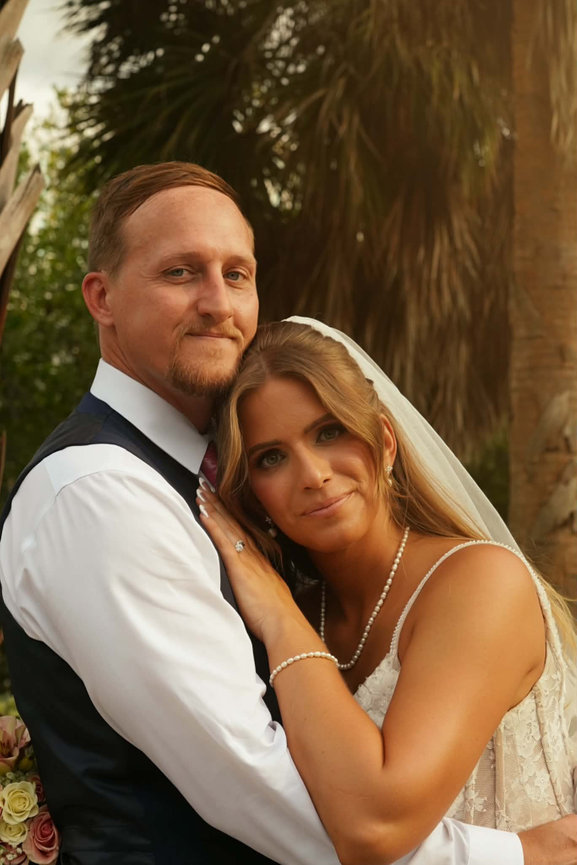 Bride and groom posing together in formal wedding attire outdoors.