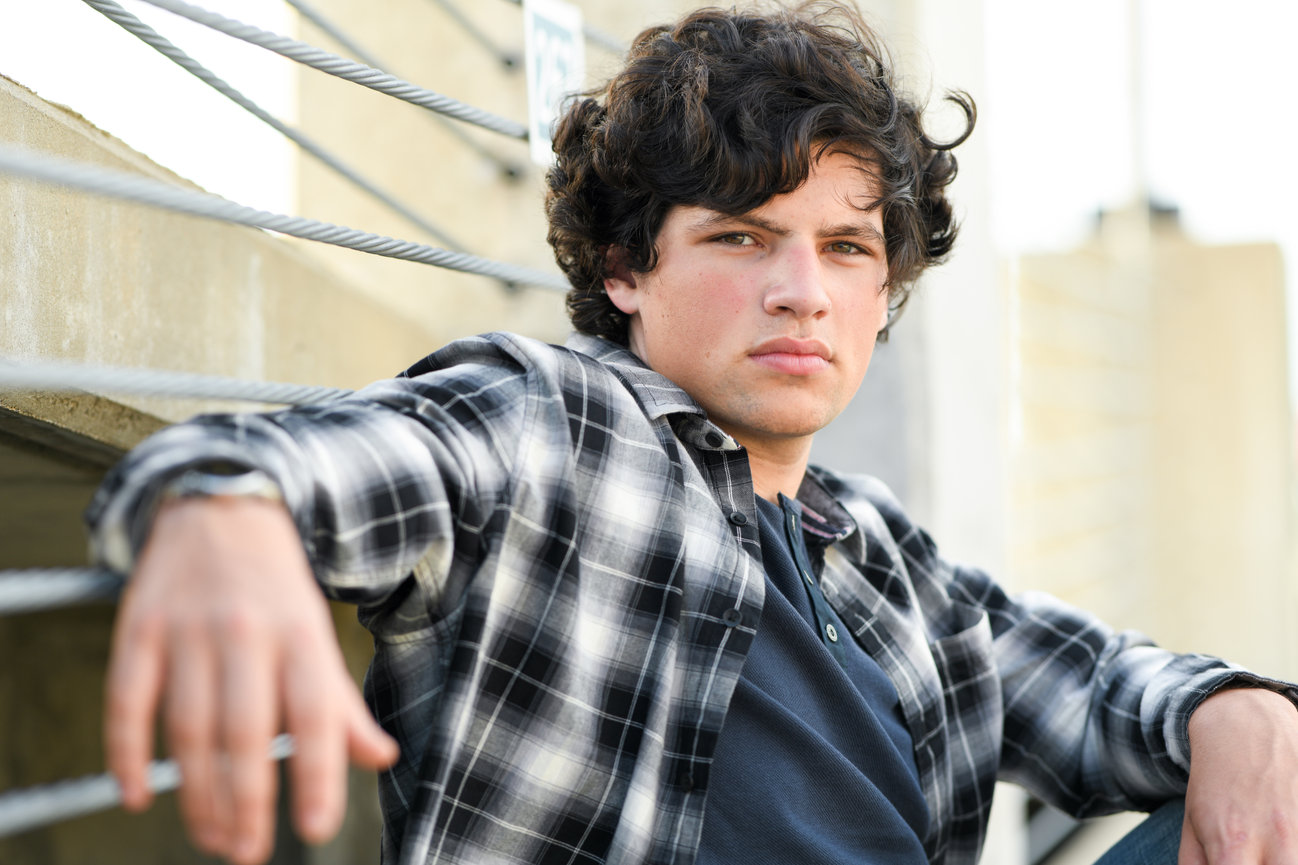 Curly and dark haired boy in a plaid shirt posing in an urban setting for his senior pictures in Dublin OH.