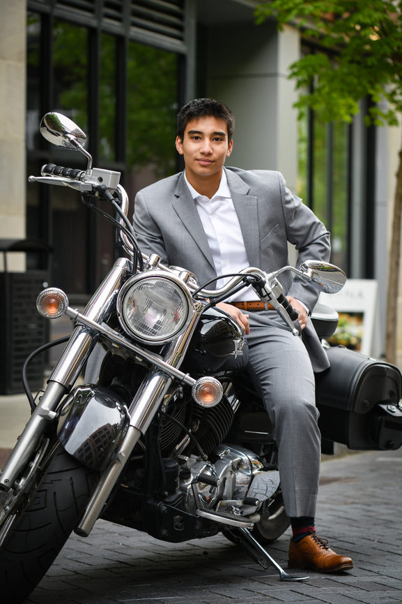 Teenage boy in a gray suit sitting on a motorcycle in an urban setting for his senior pictures in Dublin OH.