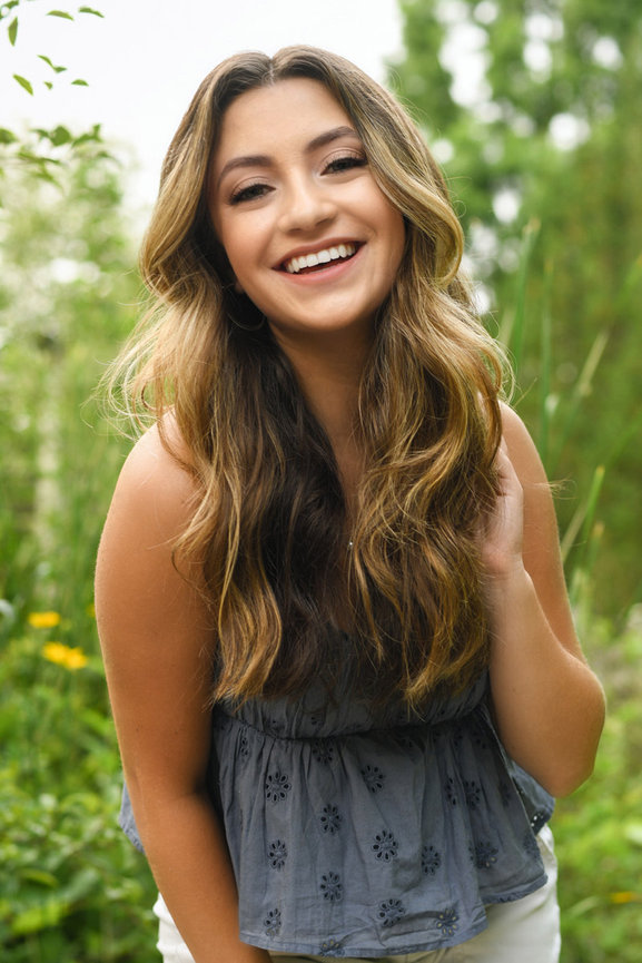 Teen girl leaning forward and laughing candidly during her senior portrait session outdoors