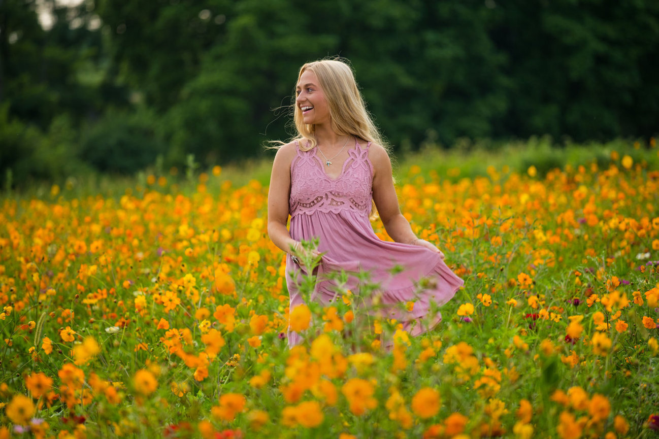 Teenage girl in a pink dress twirling in a field of orange and yellow poppies for senior pictures in Dublin OH.