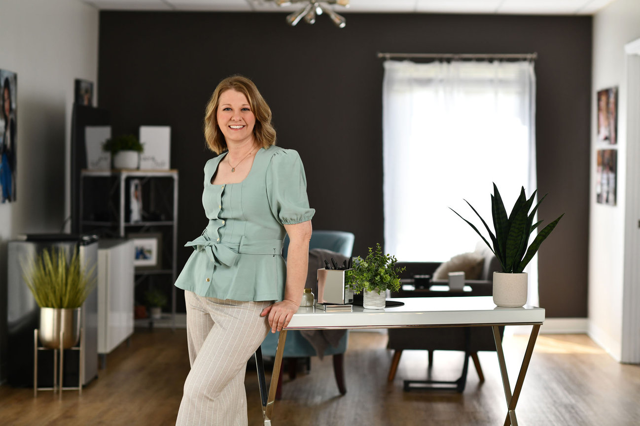 Female Professional leaning on a desk in a modern office with plants and photos.